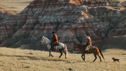 2 riders in badlands with a dog