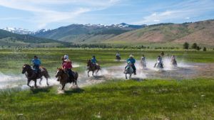 Hunewill Ranch riders splashing through water on horses