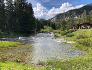Creek and cabins with green river banks and mountains