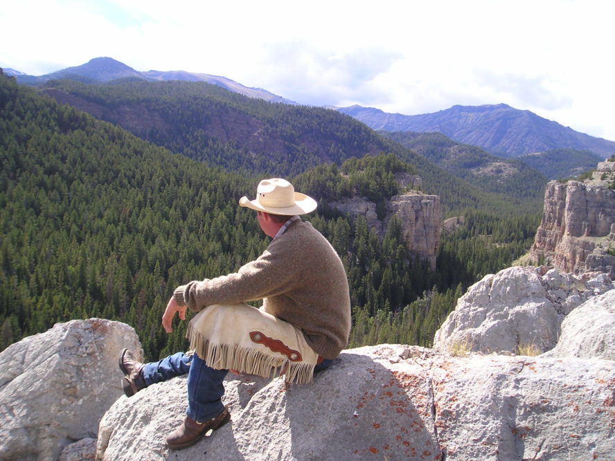 cowboy sitting on rocks overlooking a big mountain canyon