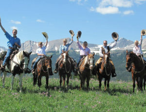 A family on horses raising their hats at Covered Wagon Ranch