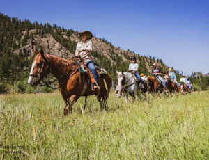 Trail ride through green field at Crossed Sabres Ranch