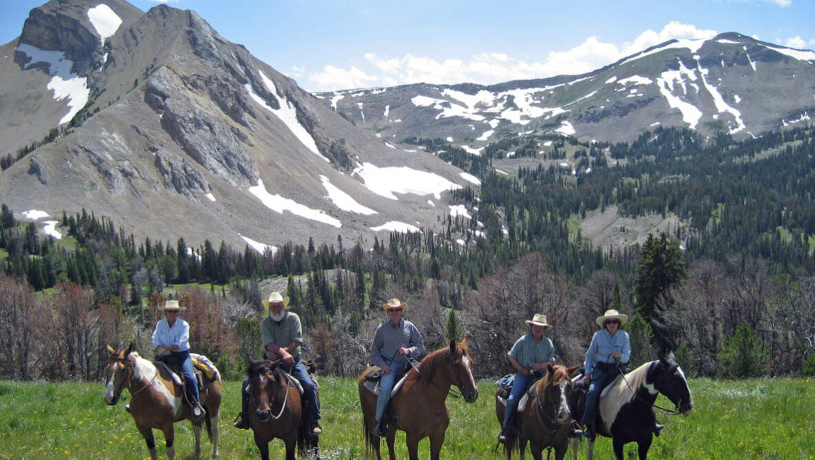 Guests on horses in a line in front of mountains at Elkhorn Ranch Montana