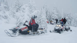 Guests snowmobiling on a snowy trail at Rich's Montana Guest Ranch