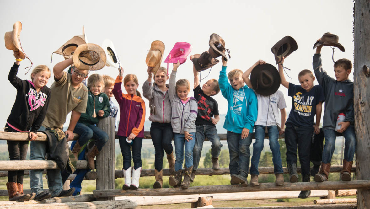 Kids in a line waving their cowboy hats in the air at Triangle X Ranch