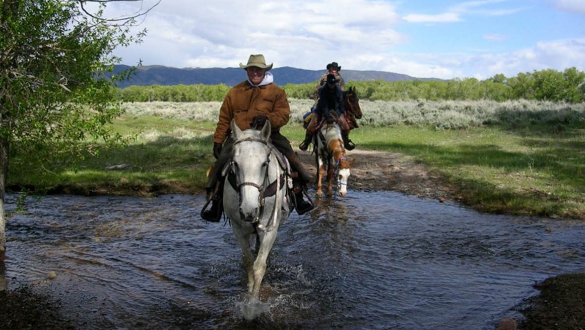 Two people on horses crossing a creek at Vee Bar Ranch