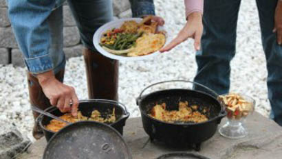 People serving food out of cast iron pots