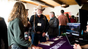 Older man in cowboy hat chatting with someone at a convention table
