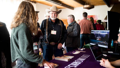Older man in cowboy hat chatting with someone at a convention table